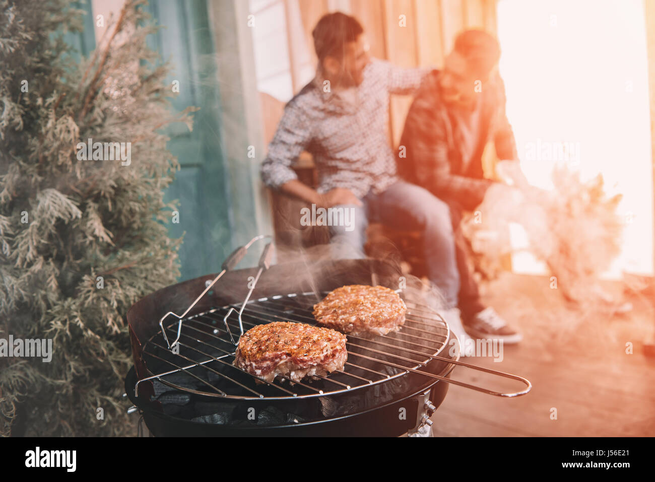 glückliche junge Freunde machen Grill auf Veranda mit Gegenlicht Stockfoto