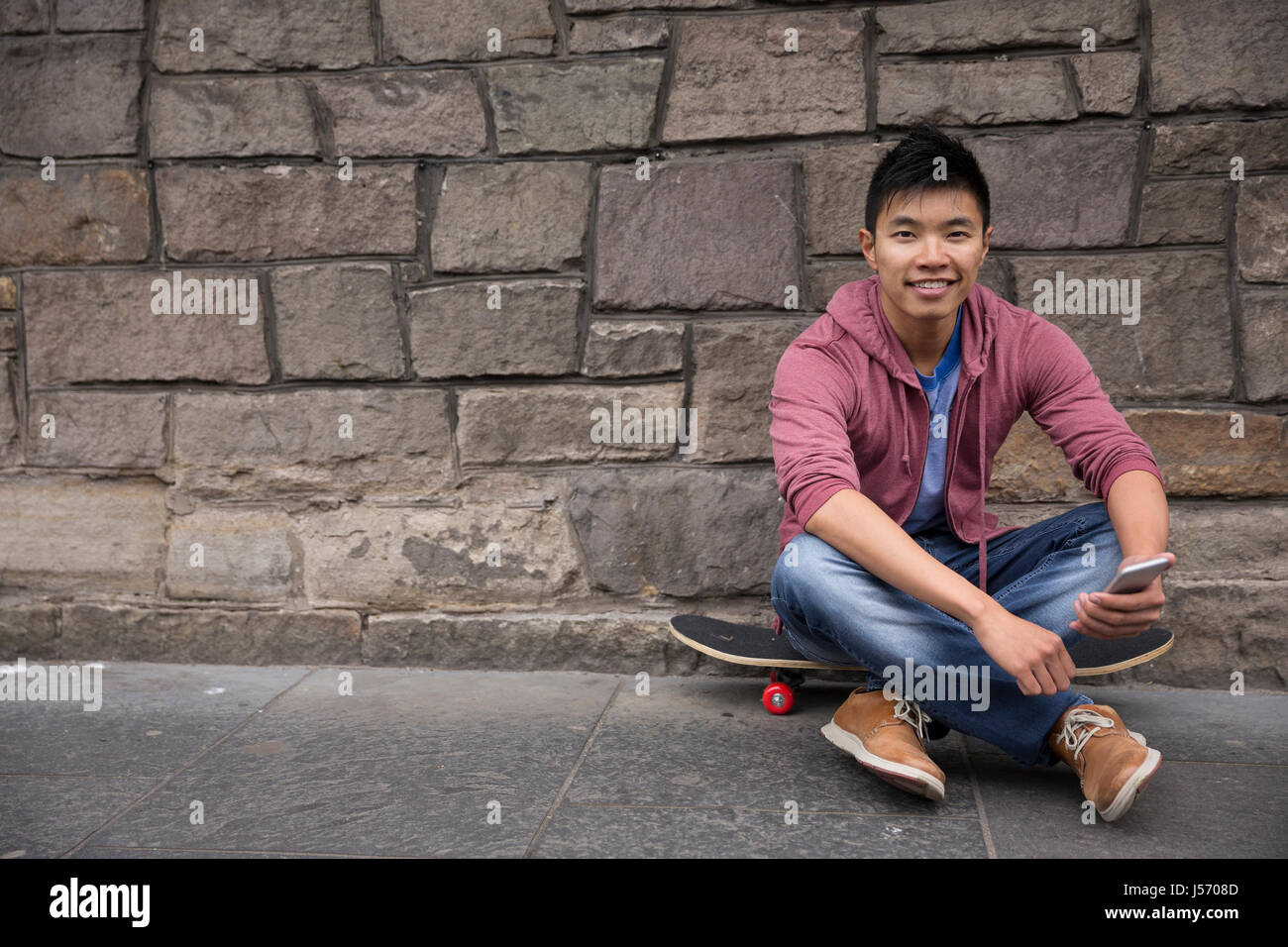 Porträt von einem asiatischen Mann mit seinem Smartphone und hält seinem Skateboard. Im Stadtstraße stehen im Freien. Stockfoto