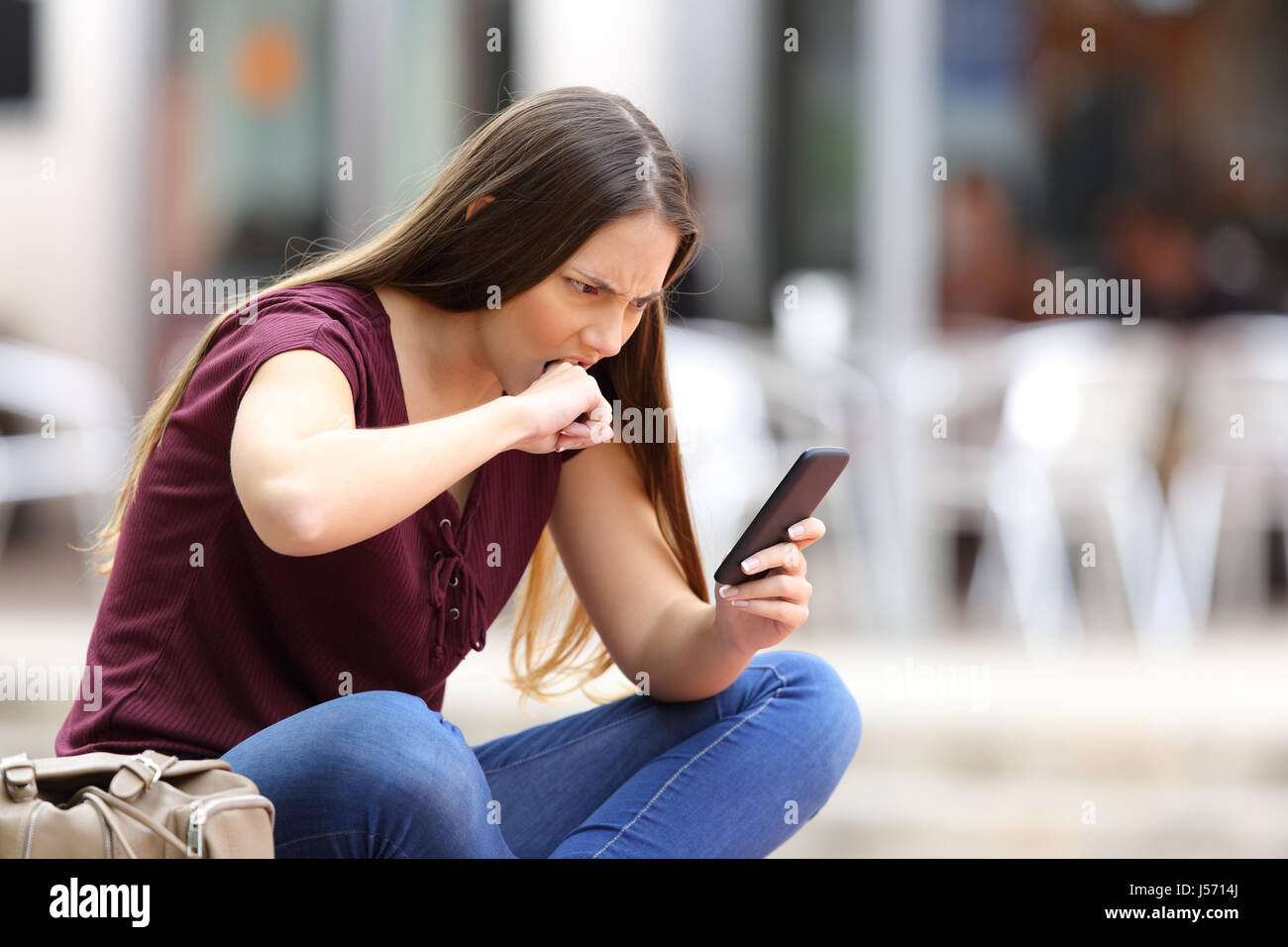 Böse Frau Empfang falsche Inhalte online in einem Mobiltelefon in einer Bank auf der Straße sitzen Stockfoto