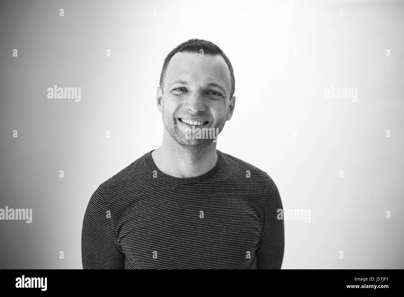 Schwarz / weiß Studioportrait lachender jungen Erwachsenen europäischen Mann über weiße Wand Stockfoto