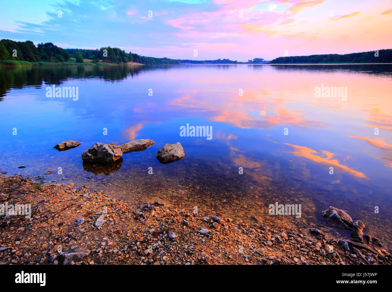 See in der warmen Dämmerung mit steinigen Strand und fuzzy Wolken spiegeln sich in Wasser. Polen, Woiwodschaft Świętokrzyskie, Cedzyna. Stockfoto