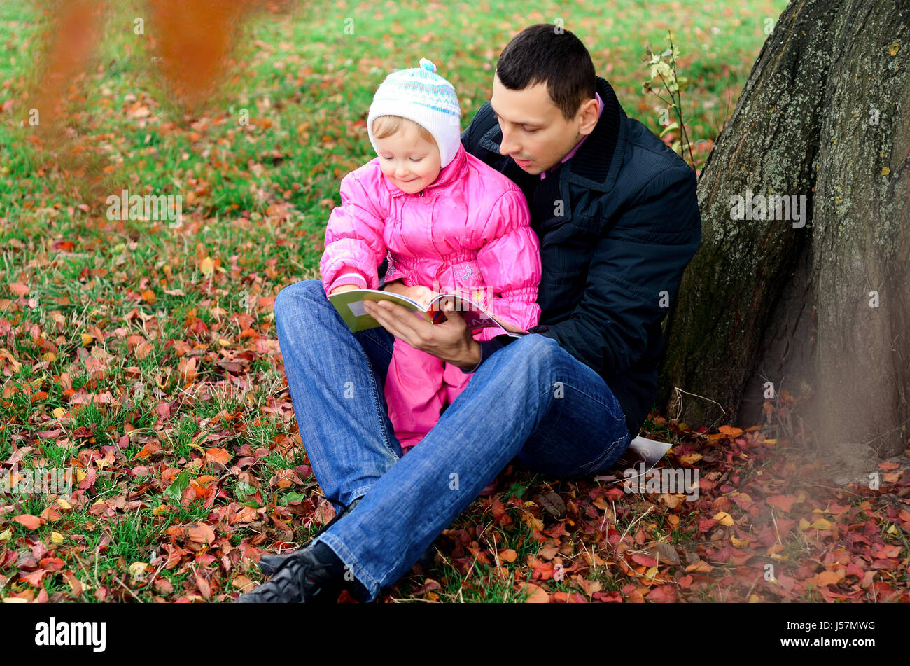 Vater und Tochter sitzen unter einem Baum fallen. Stockfoto