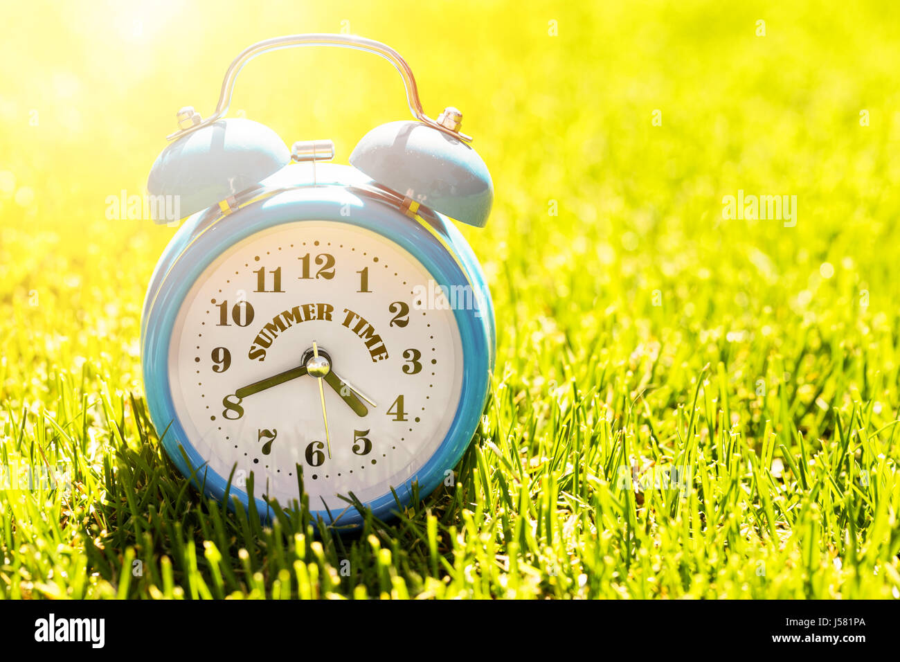 Sommer-Urlaubszeit - Wecker im grünen Rasen an sonnigen Tag Stockfoto