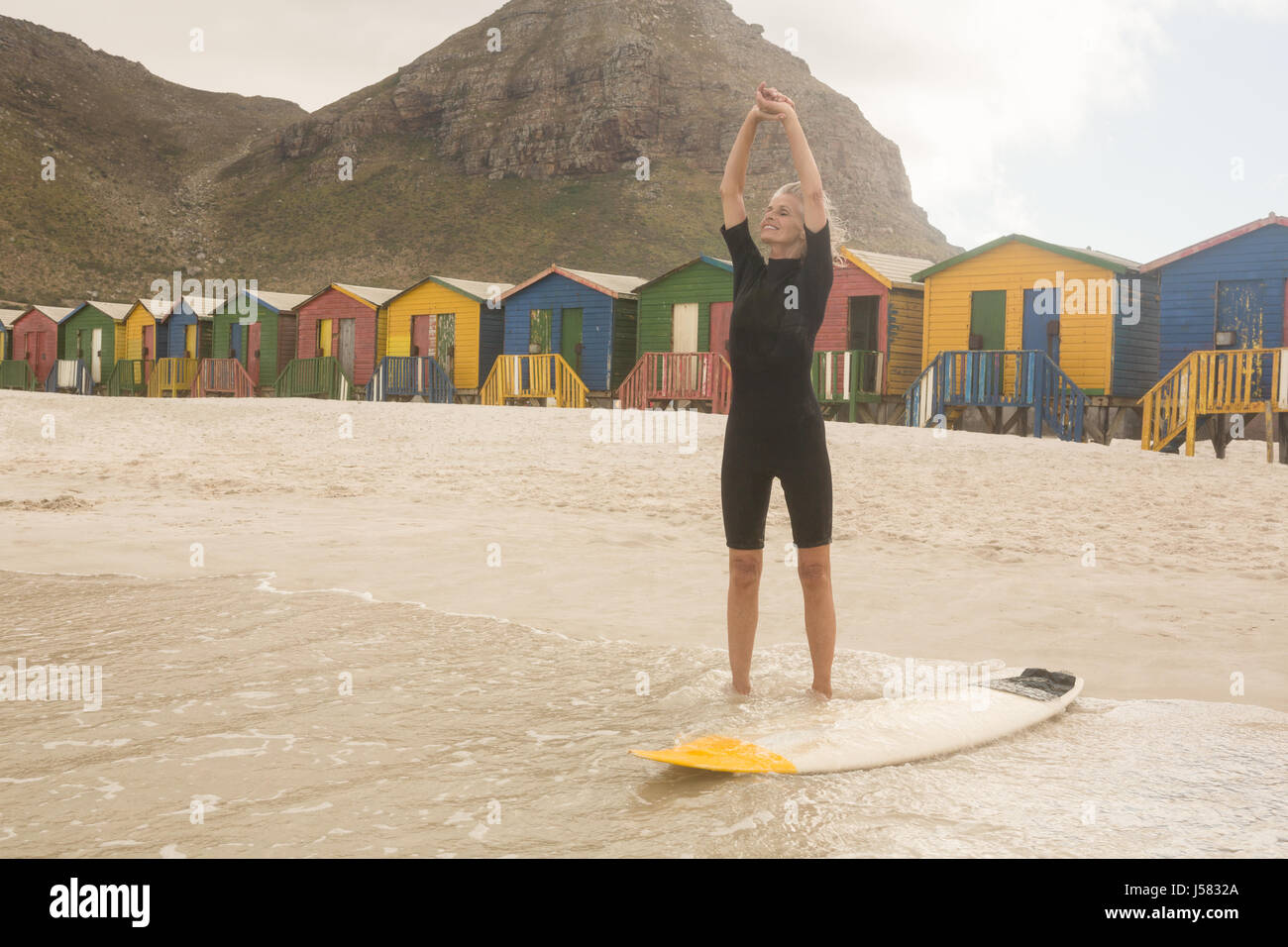 Frau ausdehnen, während sie von Surfbrett stehend gegen Hütten Stockfoto