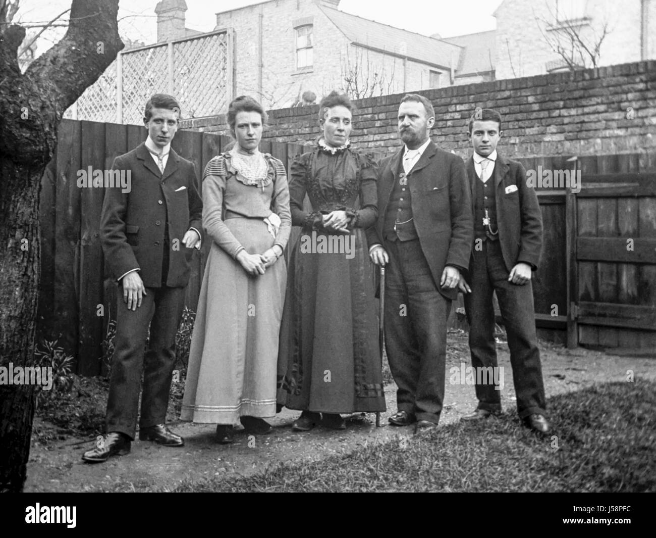 In voller Länge Portrait eines Edwardian Familie Gruppe von fünf Erwachsene zusammen im Garten eines Hauses stehen. Ein Mann kann mit Blick auf die Mauer zwischen den beiden Damen gesehen werden. Fotografiert in 1905, die die Gruppe aus zwei Frauen und drei Männer besteht. Stockfoto