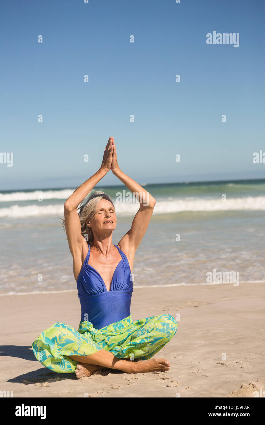 Ältere Frau, die Yoga praktizieren, während der Sitzung gegen Meer am Strand Stockfoto