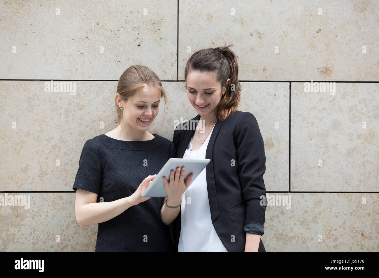 Zwei kaukasischen Geschäftsfrauen mit digitalen Tablettcomputer, Marmor Wand gelehnt. Stockfoto