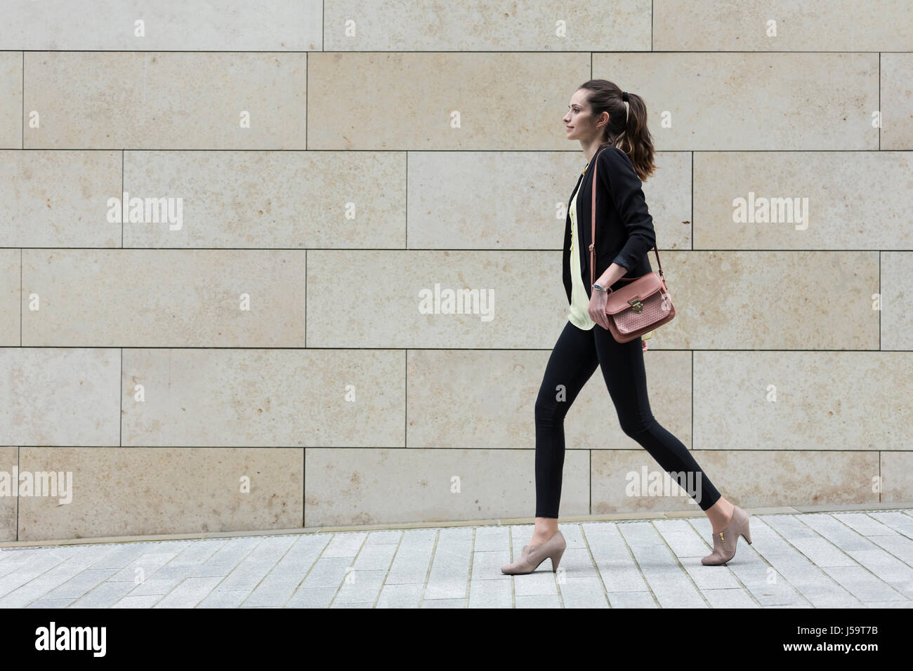 Seitenansicht des kaukasischen Geschäftsfrau zu Fuß auf Stadtstraße vor modernen Marmorwand. Stockfoto