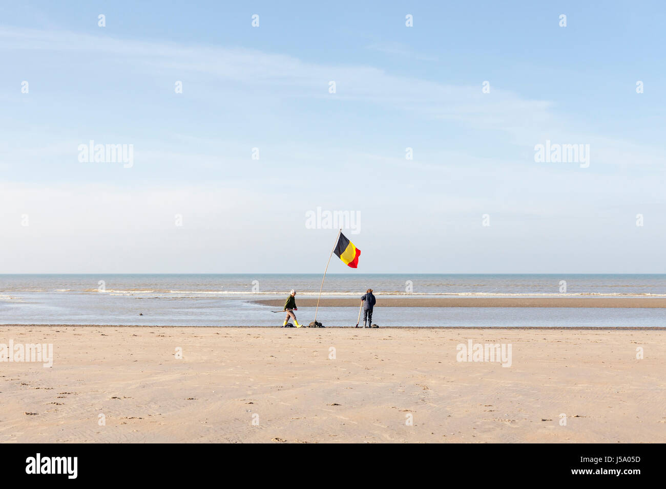 Oostduinkerke, Belgien - zwei Frauen-Anlage eine belgische Flagge am Strand. Belgische Küste. Stockfoto