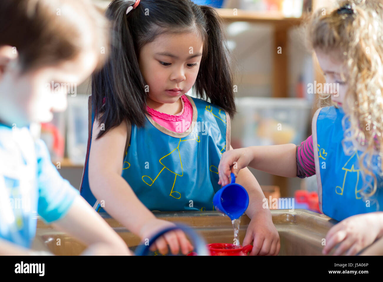 Kleinkinder tragen Schürzen sind mit einem Wasser-Tisch zusammen im Kindergarten spielen. Stockfoto