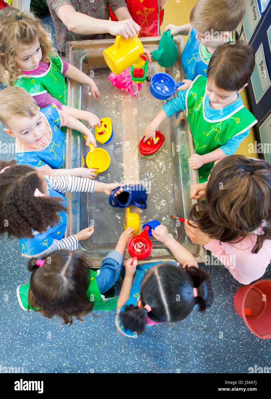 Draufsicht auf eine Klasse für Kindergarten-Kinder spielen am Wasser-Tisch. Sie sind alle Schürzen tragen und mit Plastikspielzeug. Stockfoto