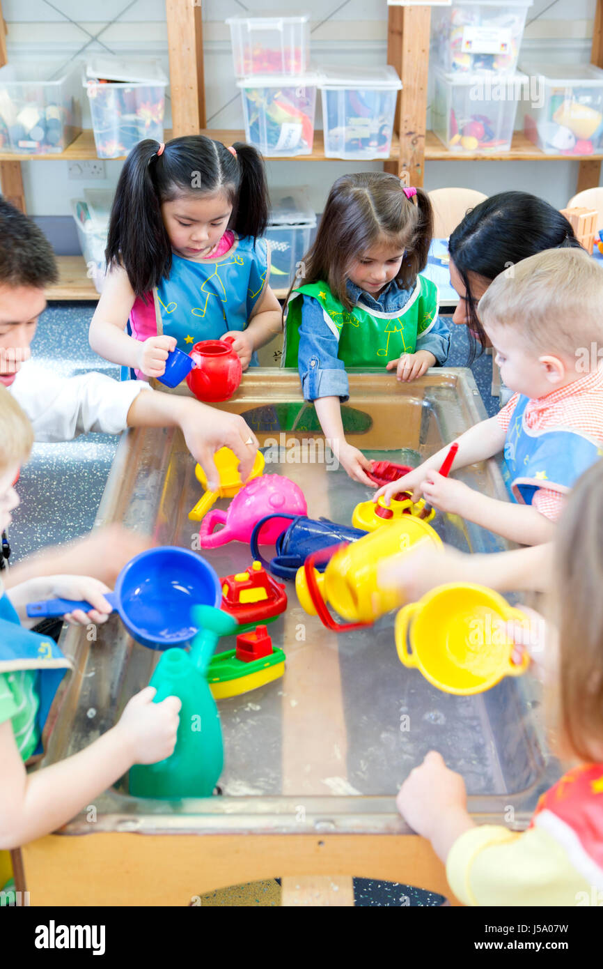 Gruppe von Kindergarten-Kinder spielen am Wasser-Tisch mit ihrem Lehrer. Stockfoto
