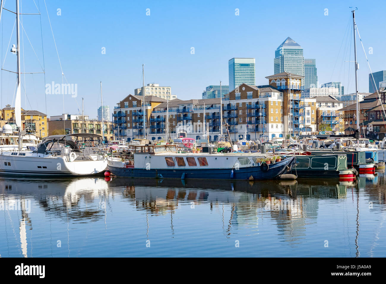 Boote und Yachten vor Anker in Limehouse Basin Marina in London mit Canary Wharf im Hintergrund Stockfoto