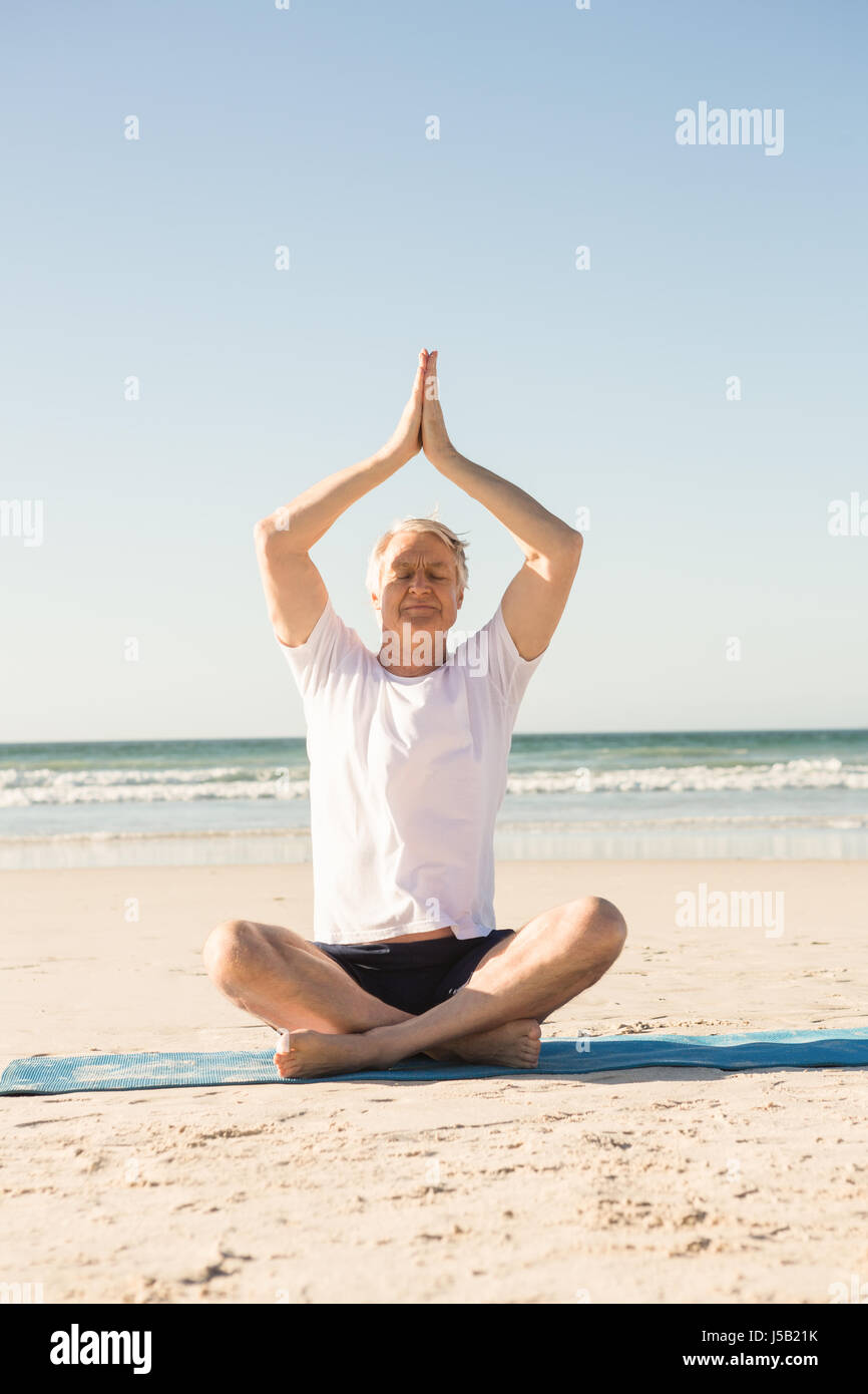 Älterer Mann sitzt auf Matten während der Meditation am Strand Stockfoto