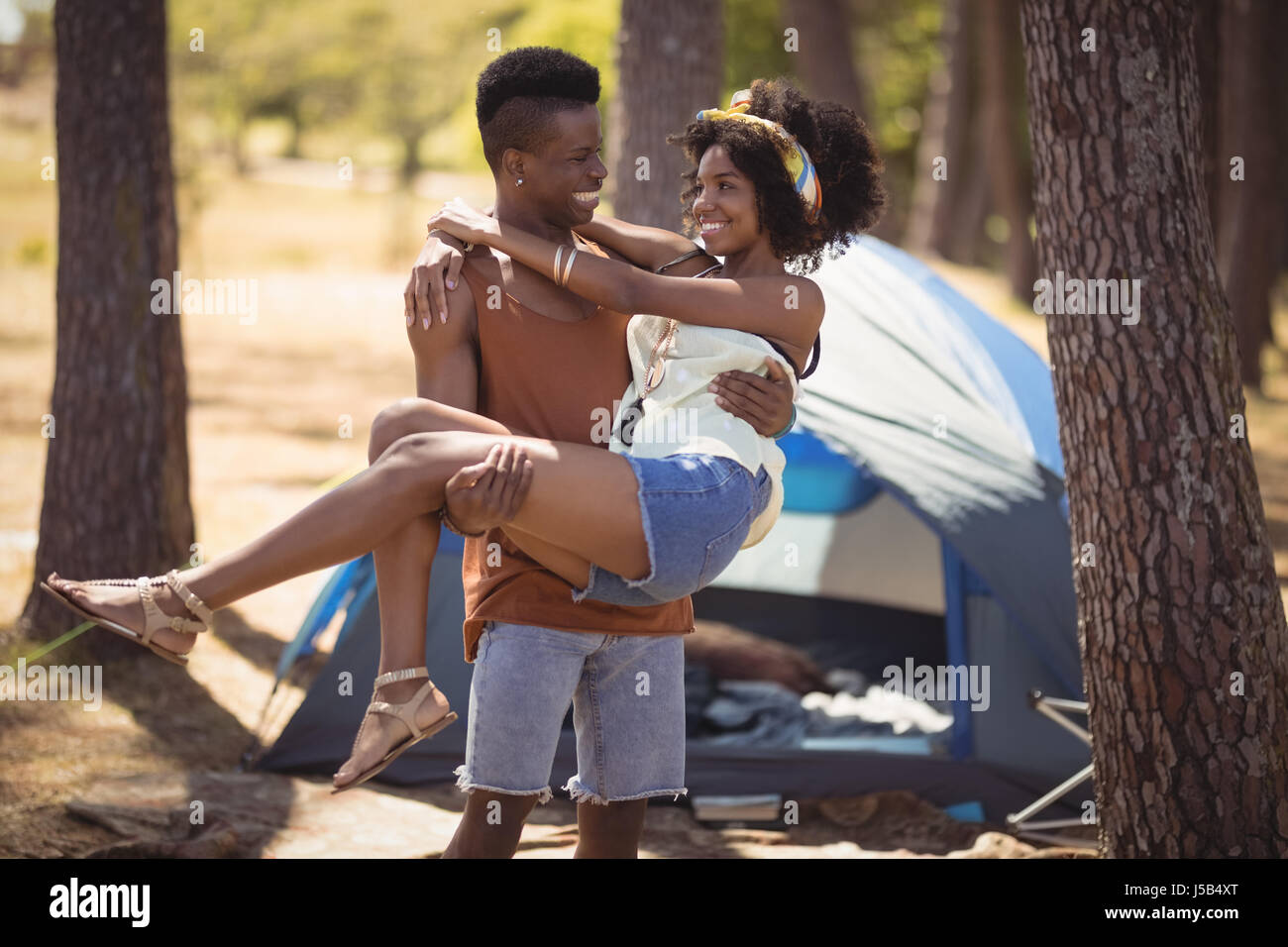 Glücklicher Mann mit Frau stehend gegen Zelt auf Feld im Wald Stockfoto