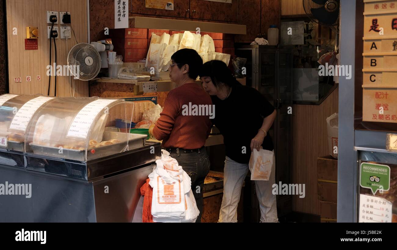 Menschen in der Schlange stehen außerhalb des Restaurants in Mongkok, Hong Kong in Shop und Verkäufer verkaufen Brötchen und Ei Torten gehen Stockfoto