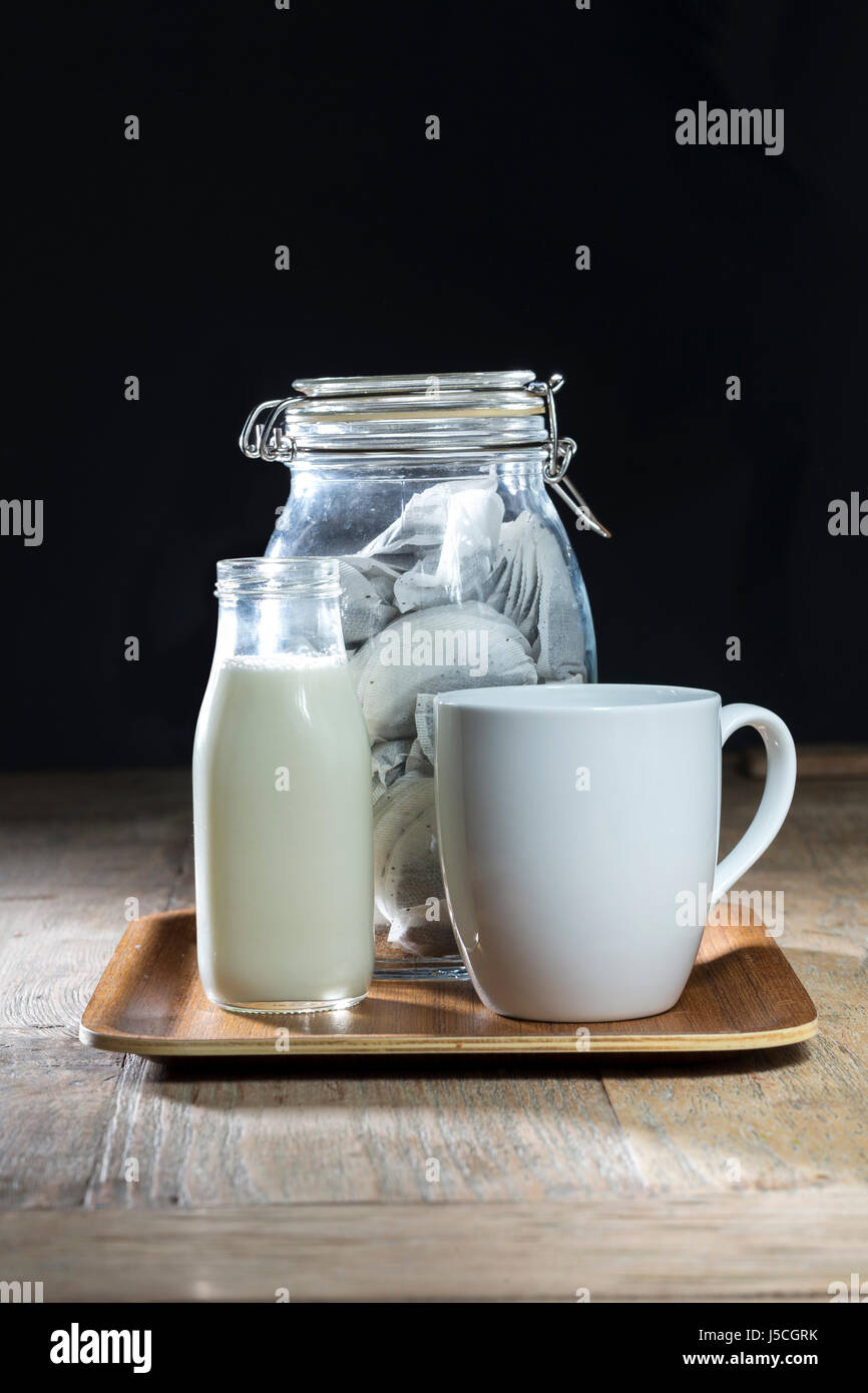 Glas mit Teebeutel, Milch und Becher auf einem rustikalen Holztisch sitzend. Stockfoto