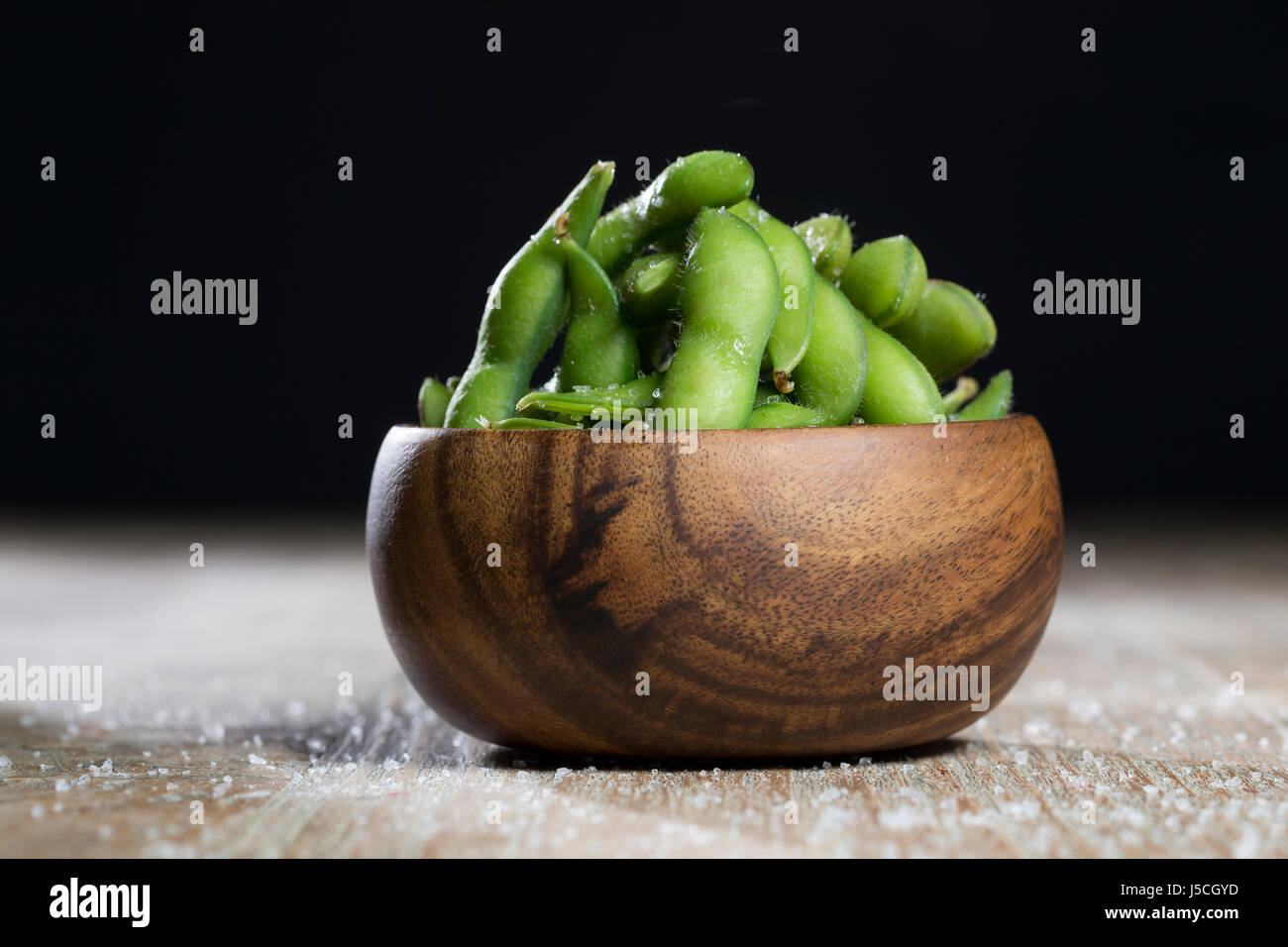 Schüssel mit Edamame sitzt auf einem rustikalen Holztisch. Stockfoto