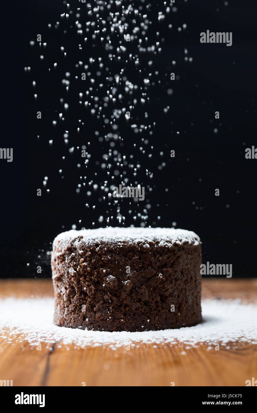 Puderzucker, fallen auf Lava Schokoladenkuchen. Schokoladenpudding auf einem rustikalen Holztisch sitzend. Stockfoto