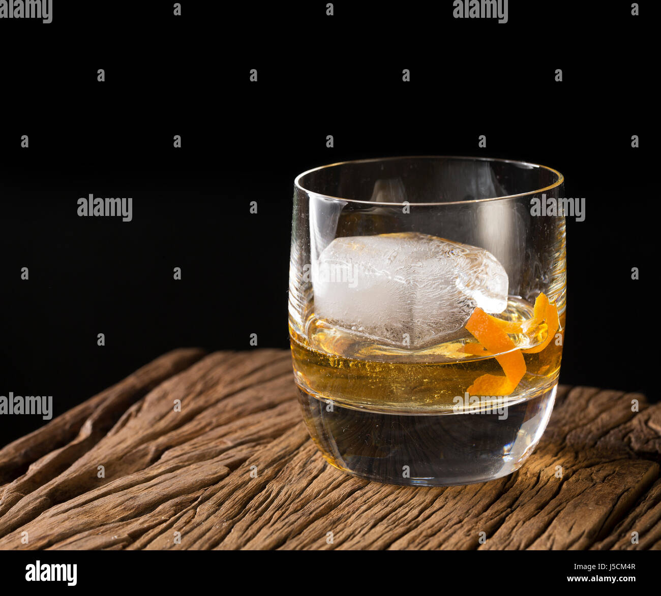 Glas von Scotch Whisky auf einem alten rustikalen hölzernen Hintergrund. Modernes Design mit einem großen Eiswürfel und Orangenschale garnieren. Stockfoto