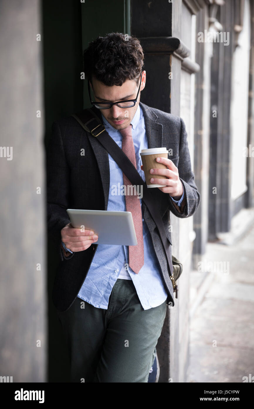 Stilvolle kaukasischen Mann, in einer Tür gelehnt Weise und mit einem Tablet-Computer. Im Freien in der Stadt. Stockfoto