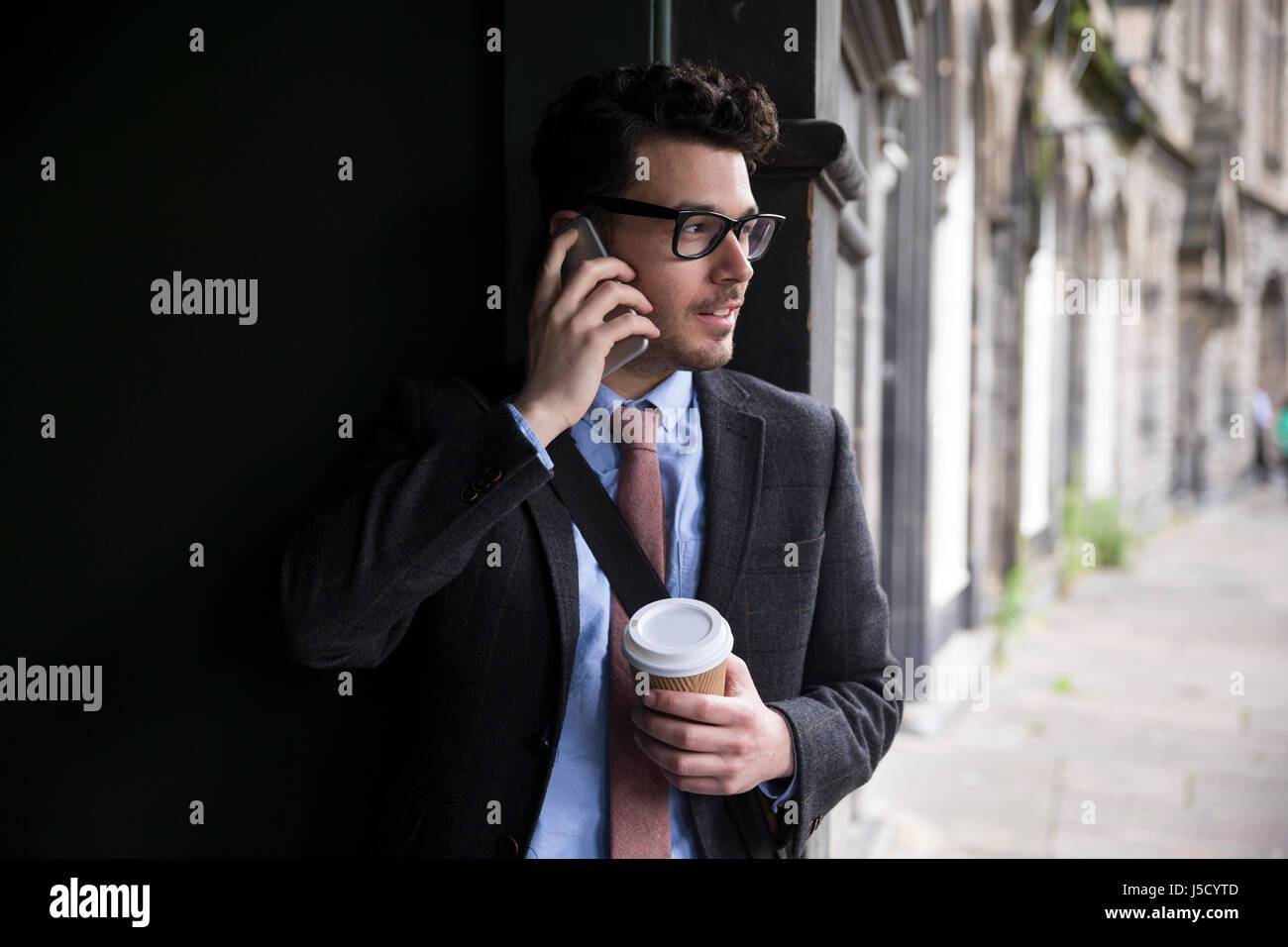 Stilvolle kaukasischen Mann, in einer Tür gelehnt Weise und mit einem Smart-Phone. Im Freien in der Stadt. Stockfoto