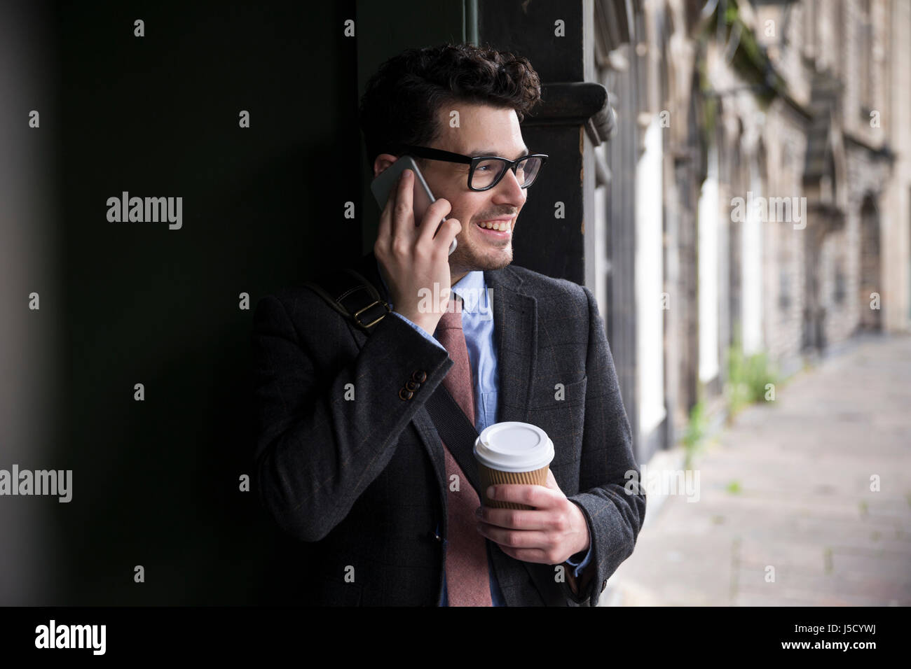 Stilvolle kaukasischen Mann, in einer Tür gelehnt Weise und mit einem Smart-Phone. Im Freien in der Stadt. Stockfoto
