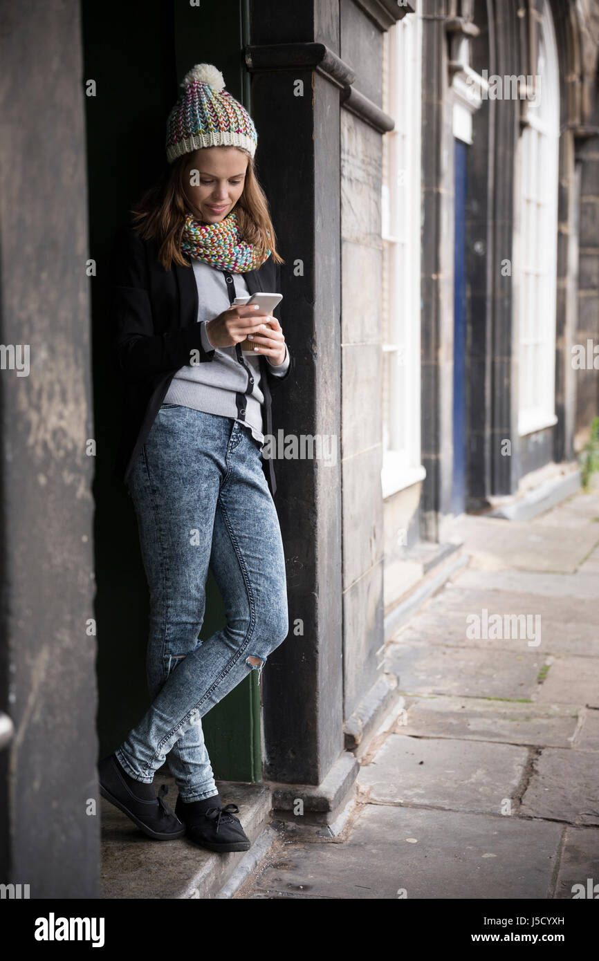 Kaukasische Frau, in einer Tür gelehnt Weise und mit einem Smart-Phone. Im Freien in der Stadt. Stockfoto
