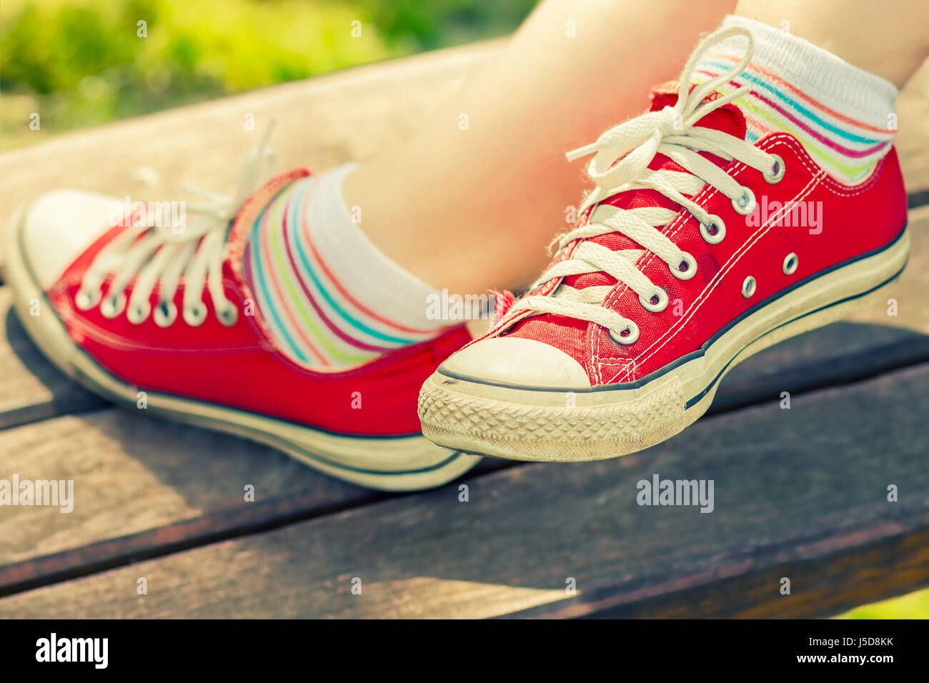Frau die Füße in einem roten canvas Sneaker mit bunten Socken, sitzen auf einer Bank Stockfoto