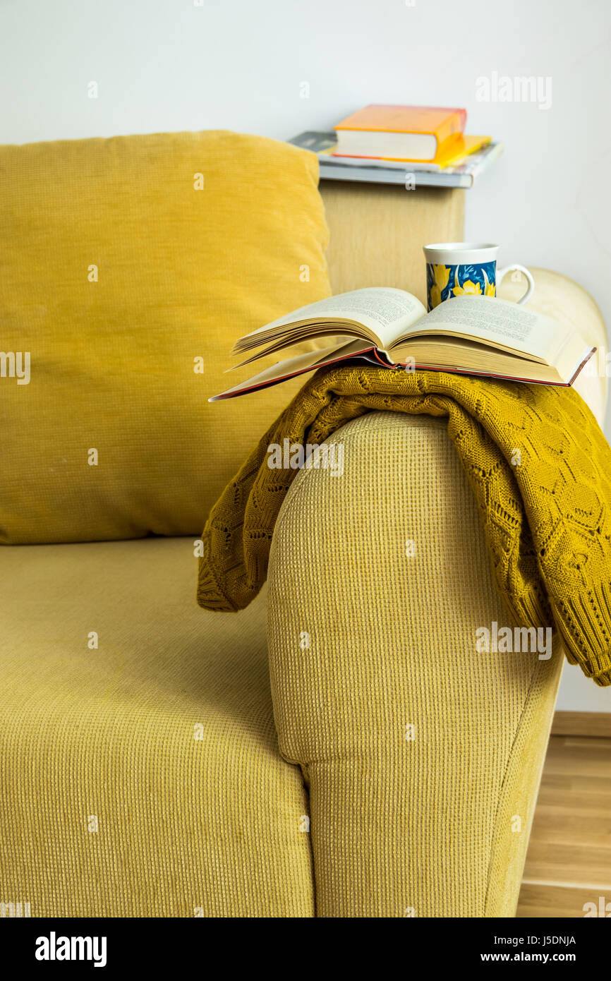 Innen gelb Cord Sofa im Wohnzimmer mit Kissen, Strickpullover, öffnen, Buch, Teetasse, gemütliche Atmosphäre, selektiven Fokus Stockfoto