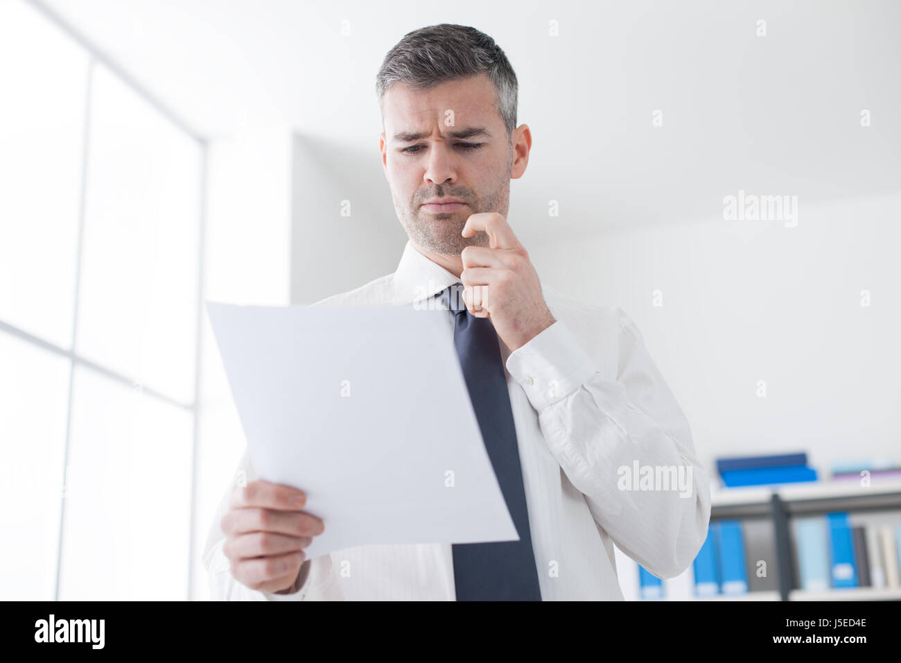 Geschäftsmann Prüfung teure Rechnungen an einem Dokument, ist er runzelte die Stirn und Kinn berühren seine Stockfoto