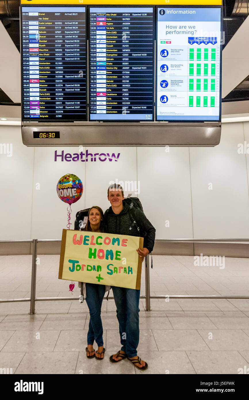 Ein junges Paar hält eine Willkommen Zuhause melden Sie nach seiner Rückkehr von der Reise, Flughafen Heathrow, London, UK Stockfoto