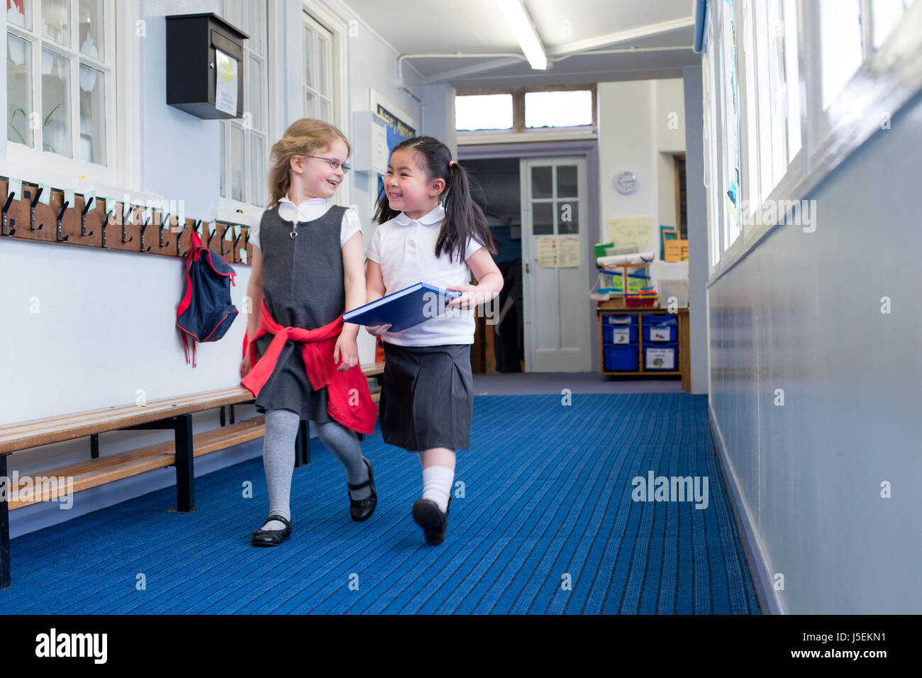Zwei weibliche Kindergarten Studenten gemeinsam gehen hinunter den Korridor. Man hält ein Buch und sie sind beide lachen im Gespräch. Stockfoto