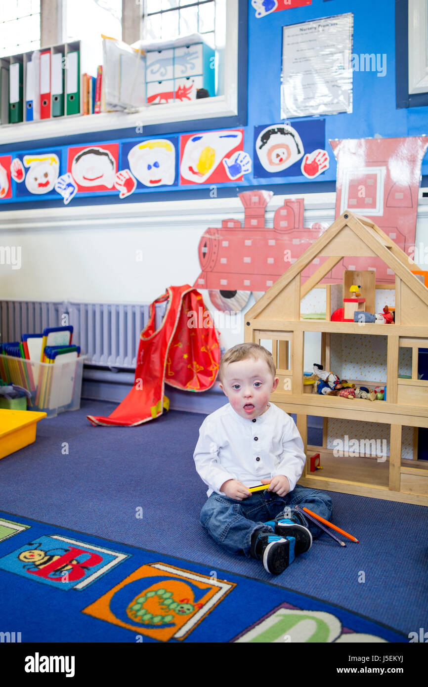 Down-Syndrom junge spielt mit Buntstifte in seinem Kindergarten Klassenzimmer. Er schaut in die Kamera. Stockfoto