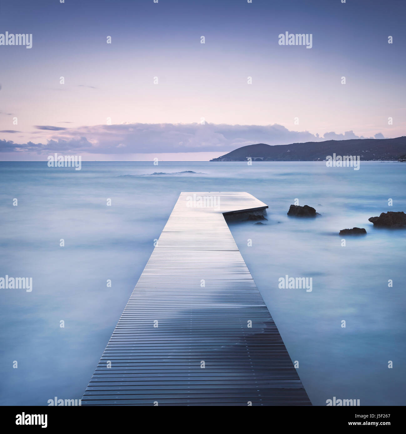 Hölzerne Pier oder Steg in der Bucht, Felsen und Meer auf dem nebligen Sunset. Langzeitbelichtung Stockfoto