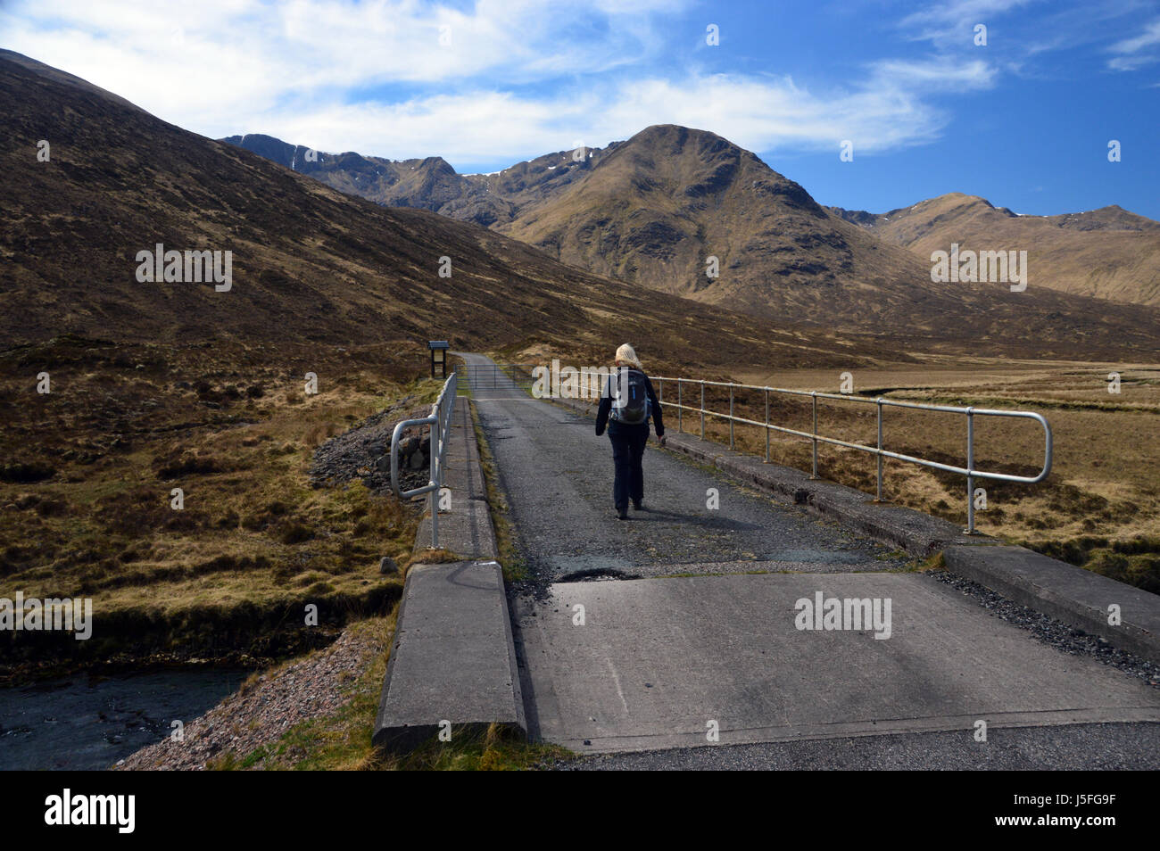 Einsame weibliche Hillwalker zu Fuß auf der Beton-Brücke über den Fluss Cluanie mit der schottischen Berge Munro Aonach Luft Chritih in Glen Shiel, Stockfoto