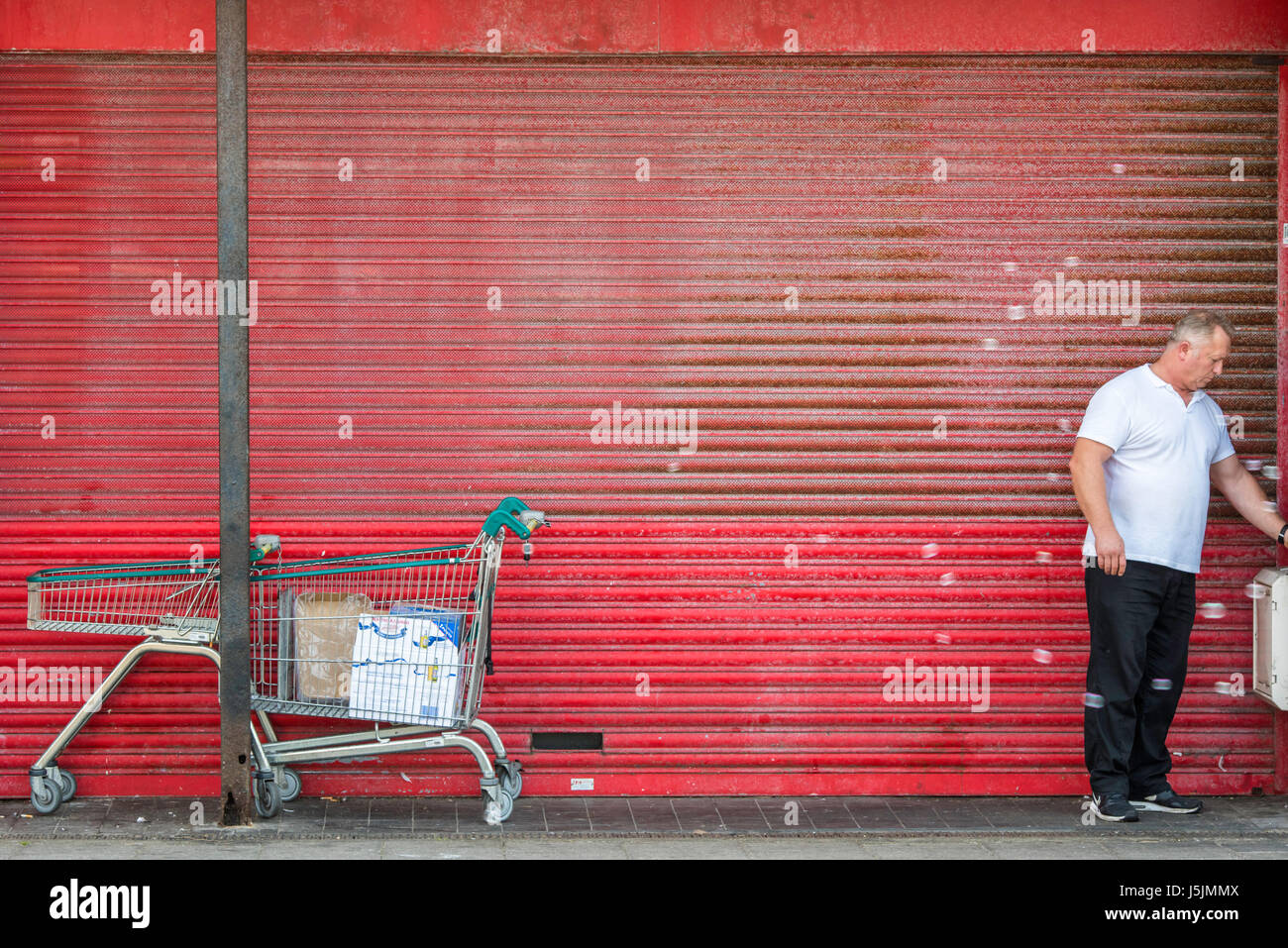 Ein Mann mittleren Alters eine Zigarette draußen ein Closed Shop roden. Der Shop roten Fensterläden sind nach unten. Stockfoto