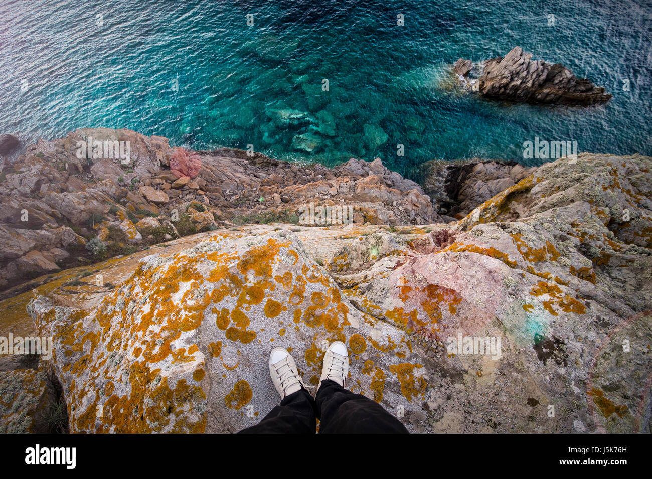 Ein Mann steht auf einem hohen Felsen von einer italienischen Küste mit dem Mittelmeer unter ihm. Porto Cervo - Costa Smeralda, Sardinien - Italien Stockfoto
