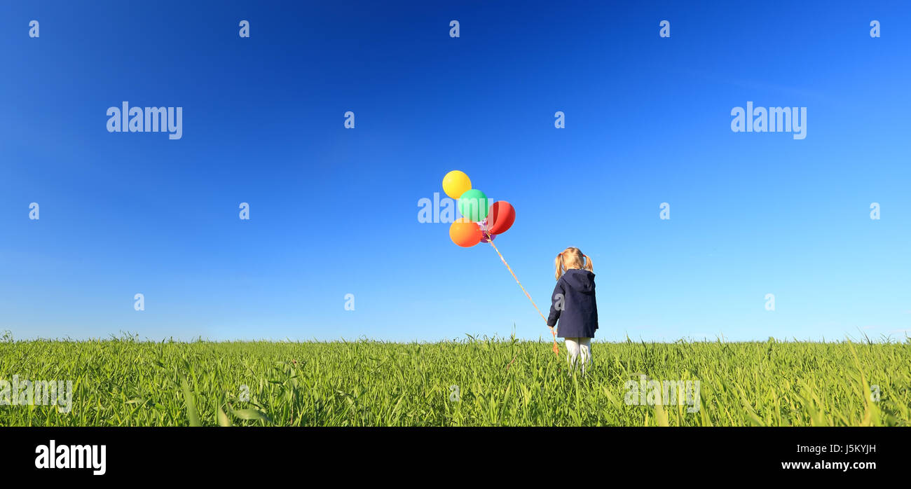 Ein kleines Mädchen mit bunten Luftballons auf blauen Himmelshintergrund. Sommer-Panorama-Landschaft mit Kind Ballons halten. Glück und Freiheit Konzept. Stockfoto