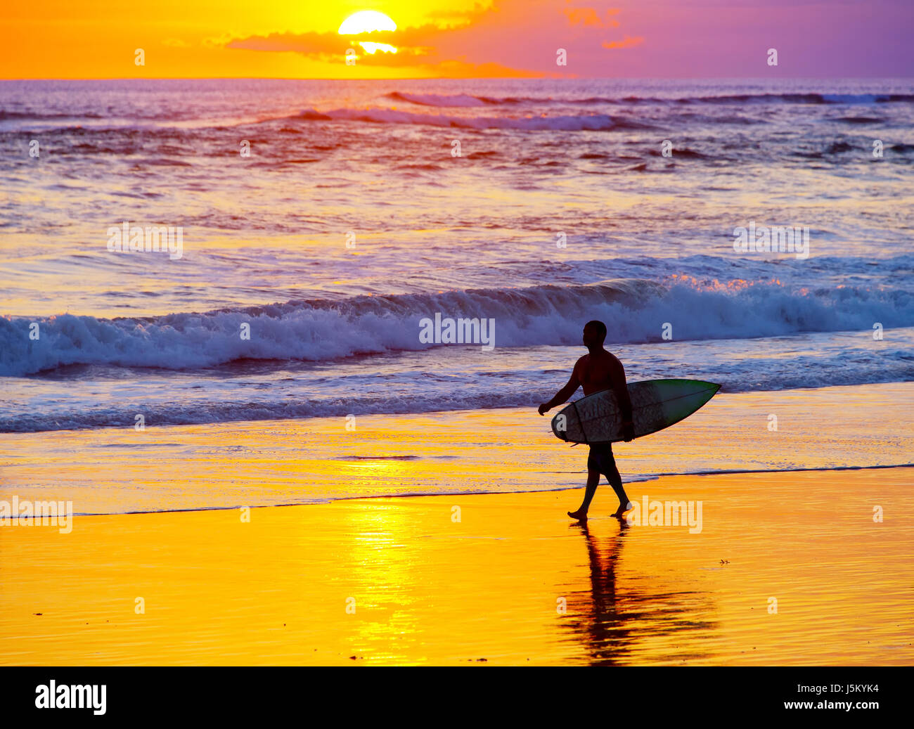 Surfer mit Surfbrett zu Fuß am Strand bei Sonnenuntergang. Insel Bali, Indonesien Stockfoto