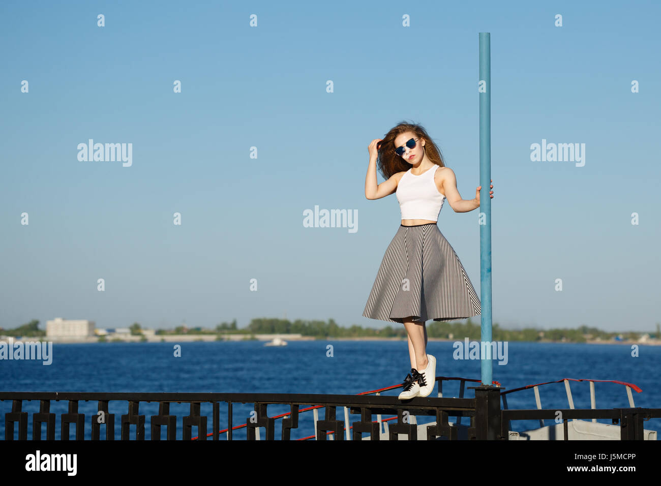 Junge attraktive Mädchen Hipster tanzen auf der Pole. Sie ist ein Top, einen Rock und eine Sonnenbrille tragen. Das Konzept des Lebens in Bewegung. Stockfoto
