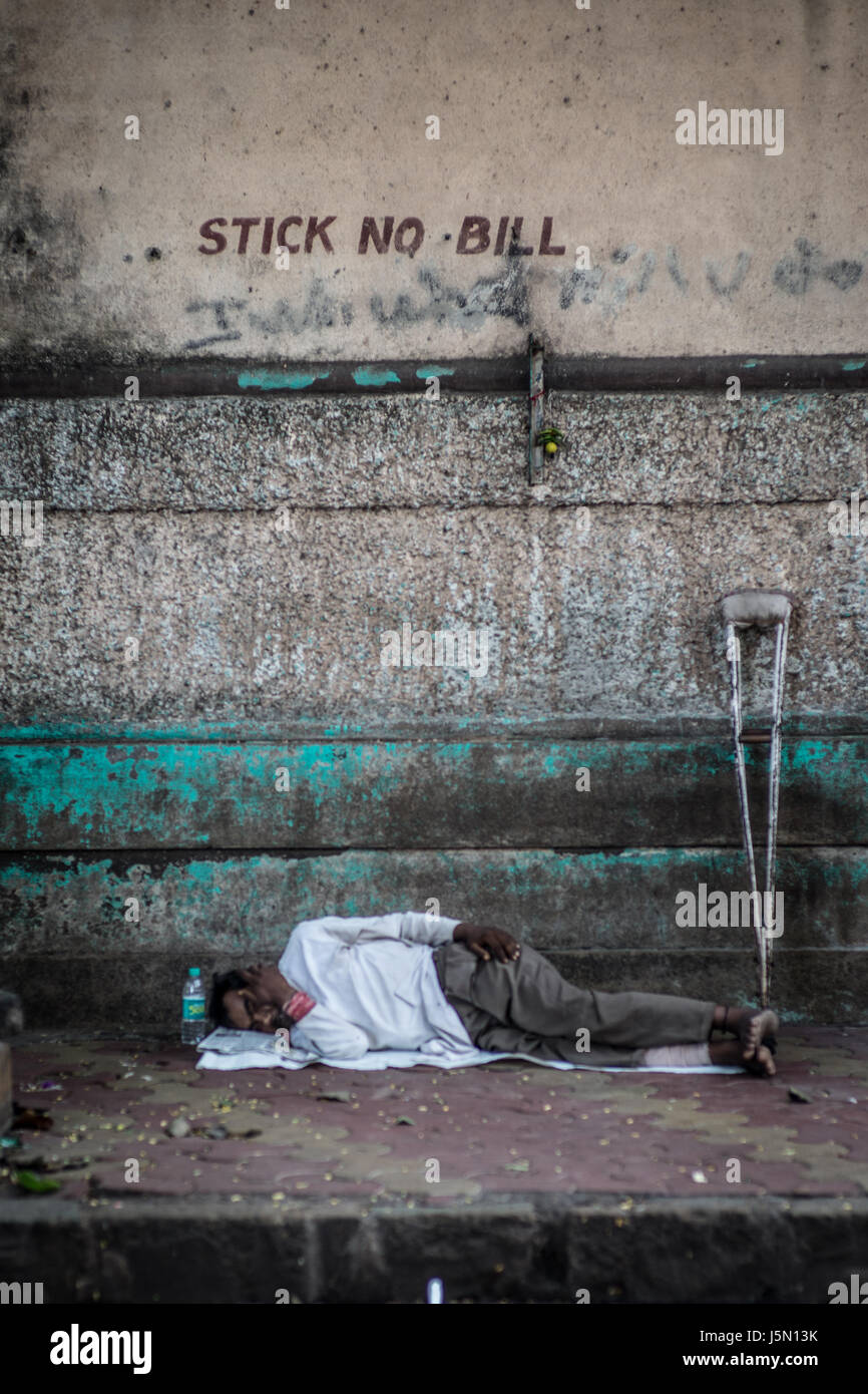 Ein Mann schläft während der heißen nachmittags neben einer Wand auf einer Straße in Mumbai, Indien Stockfoto