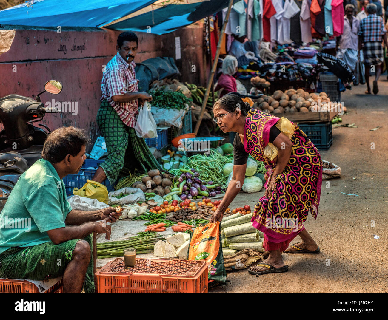Dame Kleider in der traditionellen indischen Kleid kaufen Gemüse am Markt von Mann in Lungi Tee trinken in Mallappally, Kerala, Indien gekleidet. Stockfoto