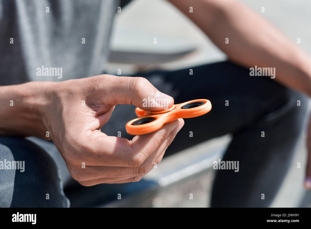 Nahaufnahme eines kaukasischen Jünglings mit einem orange Fidget Spinner im Freien spielen Stockfoto