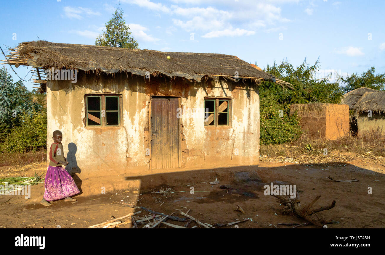 Mädchen zu Fuß Vergangenheit aufgegeben traditionell gebaut Lehmhaus mit Reetdach und Plastikplanen unter dem Rasen in einem ländlichen Dorf in Malawi, Afrika Stockfoto