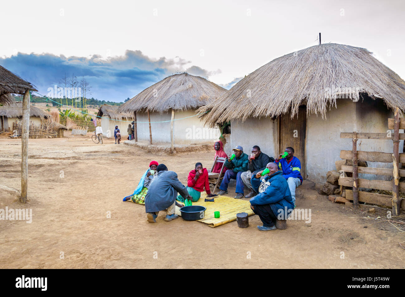 Männer und Frauen trinken Tobwa (ein vergorenes Getränk Mais) außerhalb Rasen strohgedeckte Lehmhütte in einem ländlichen Dorf in Malawi, Afrika Stockfoto