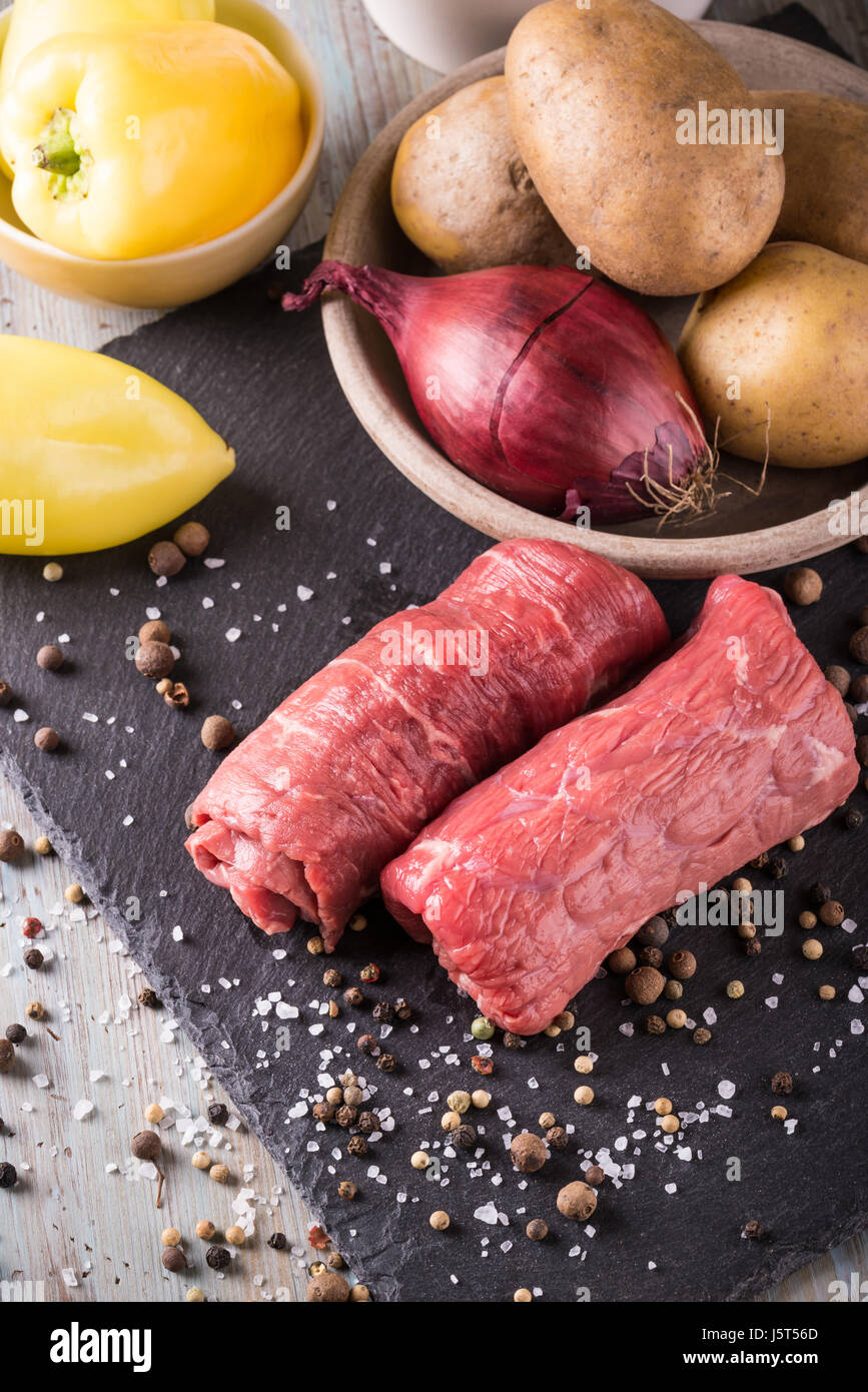Vertikale Foto mit Rindfleisch rolls. Zwei dünne Scheiben rot rohes Fleisch für Rouladen vorbereitet. Essen auf schwarzem Schiefer mit gelben Paprika, Zwiebel, roh p Stockfoto