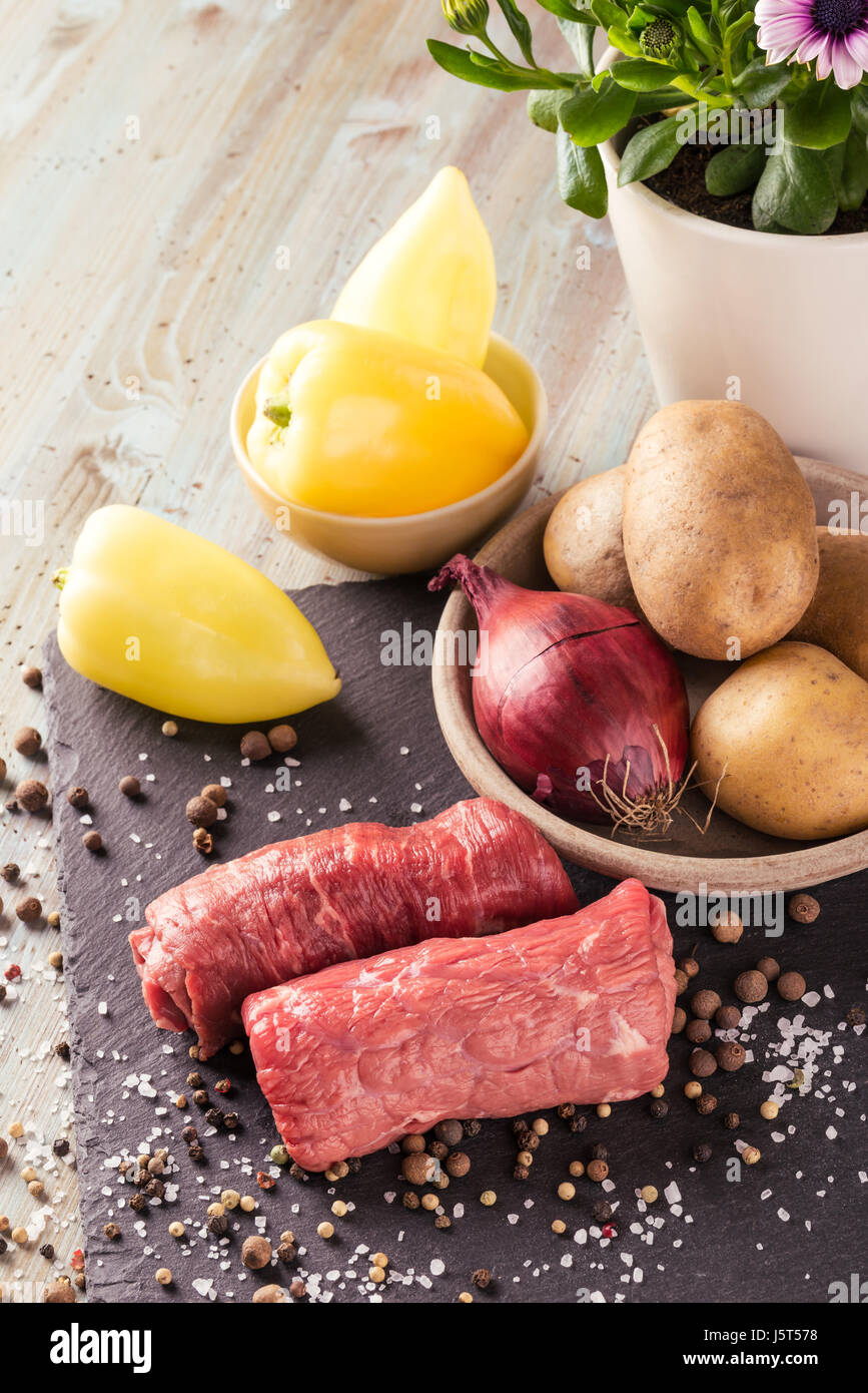 Vertikale Foto mit Rindfleisch rolls. Zwei dünne Scheiben rot rohes Fleisch für Rouladen vorbereitet. Essen auf schwarzem Schiefer mit gelben Paprika, Zwiebel, roh p Stockfoto
