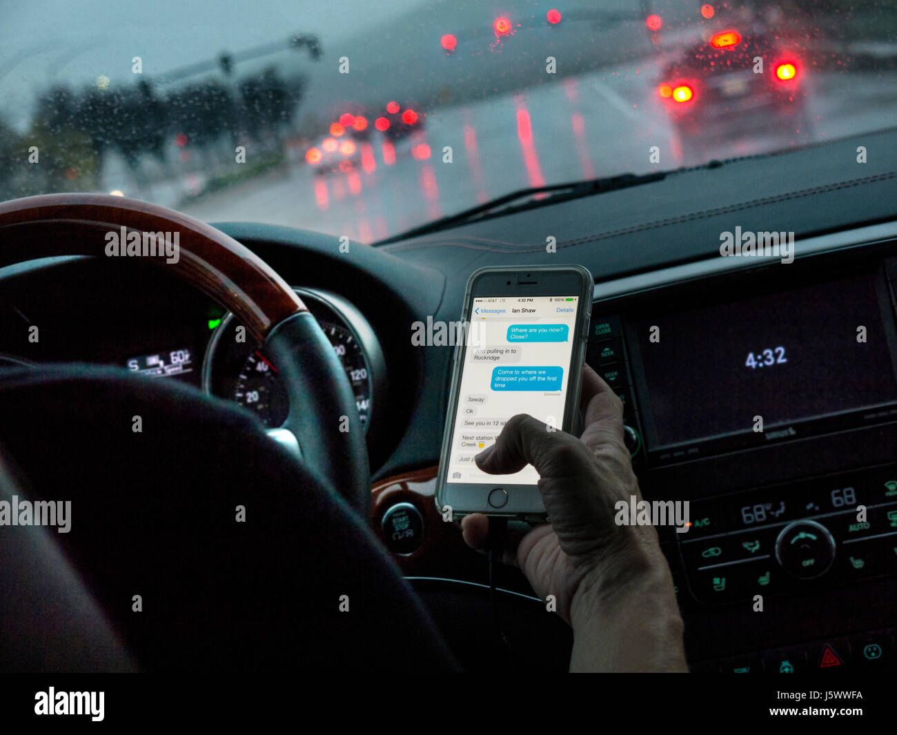 Fahrerin in l/h Fahrzeug heimlich SMS mit iPhone Smartphone während der Fahrt auf belebten nassen Straße bei Dämmerung Kalifornien USA Stockfoto