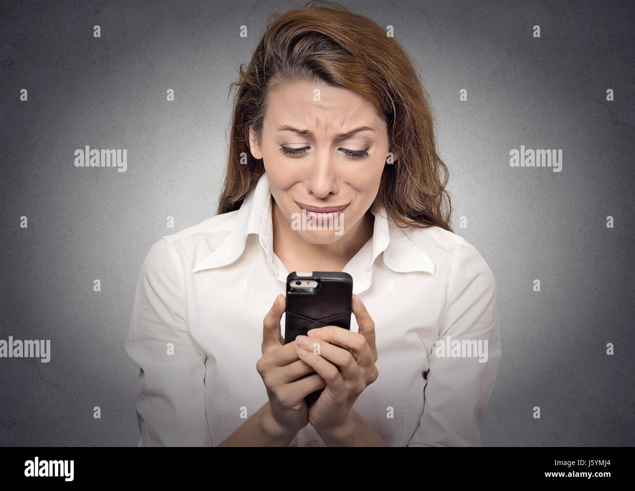 Traurig, betonte Frau ihr Handy auf graue Wand Hintergrund isoliert betrachten. Negativen Sie menschlichen Gesichtsausdruck, Emotionen, Gefühle Stockfoto